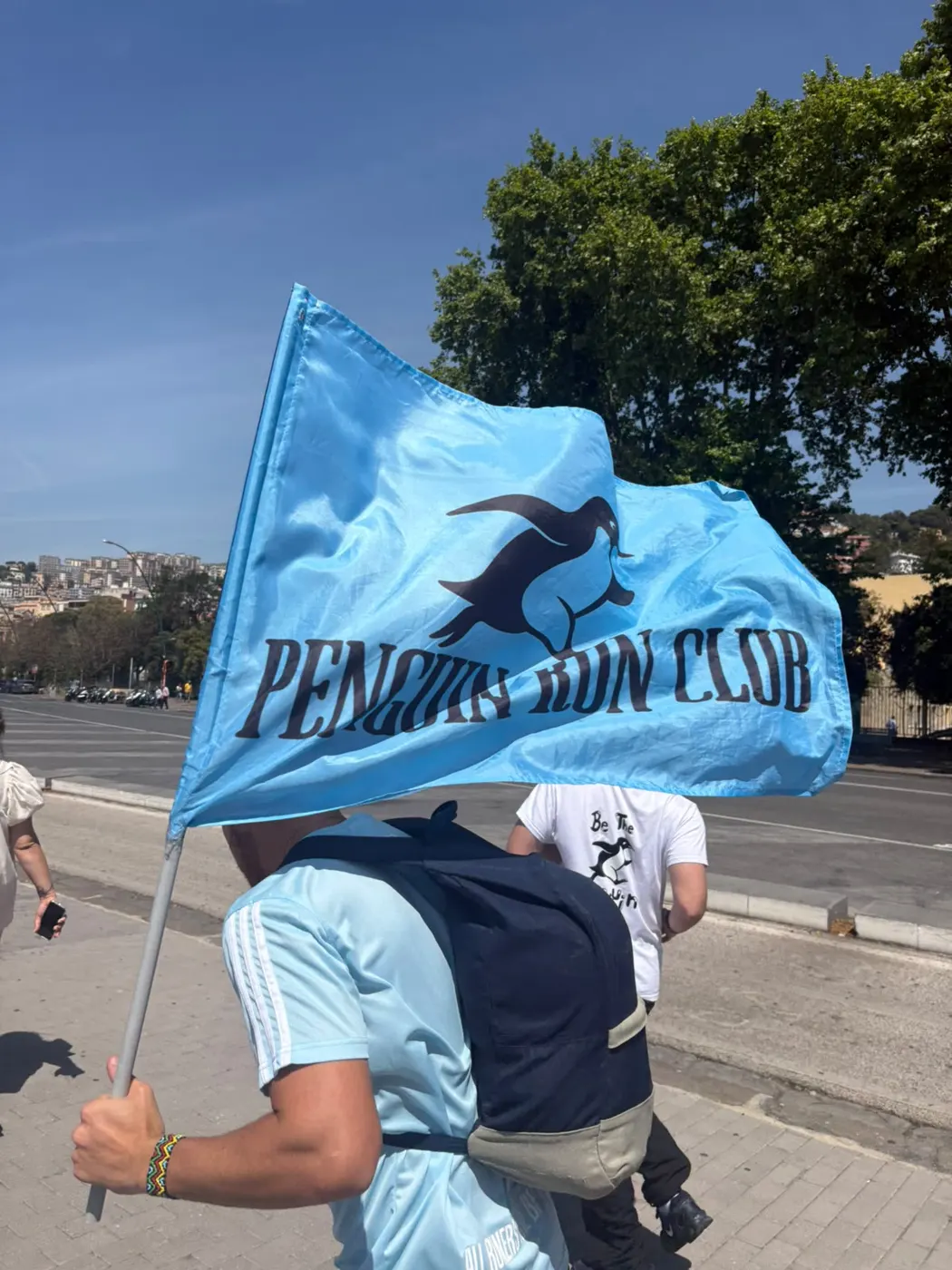 Un runner del Penguin Run Club porta la bandiera azzurra del club sul lungomare di Napoli